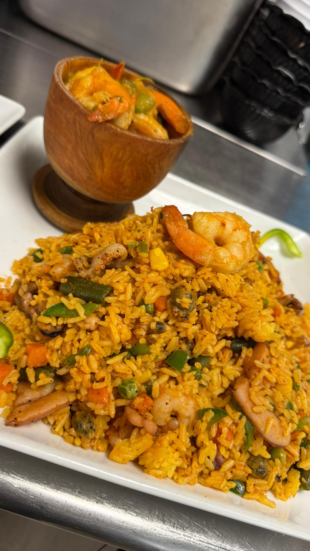 Caribe seafood rice with shrimp, calamari, and mussels alongside a wooden cup of seafood stew