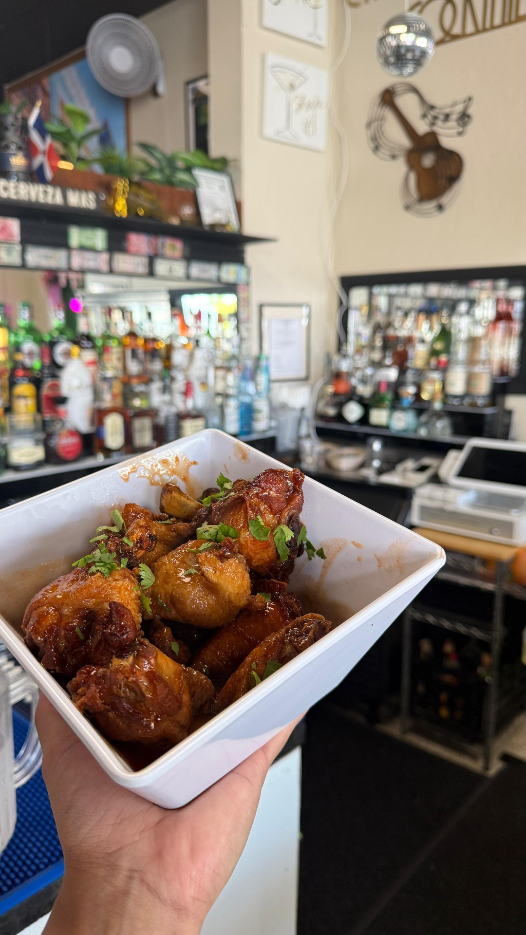 Bowl of sticky glazed chicken wings topped with cilantro at the Caribe bar