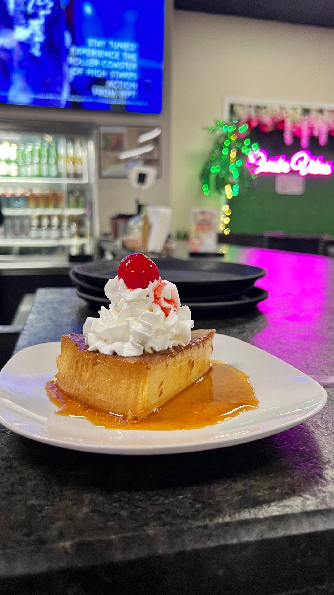 Slice of flan topped with whipped cream and a cherry at the Caribe bar with neon glow