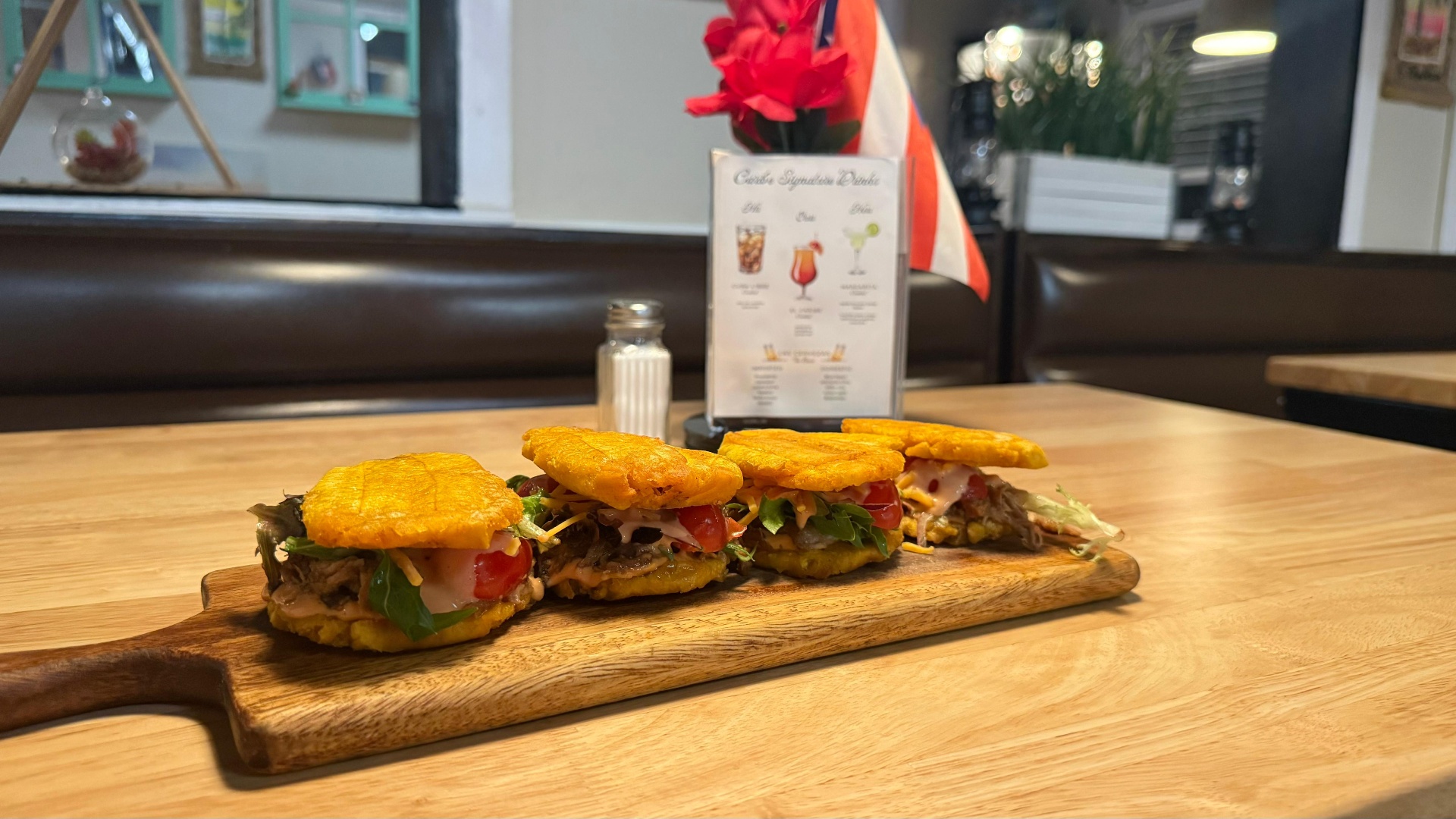 Tostones sliders with pulled meat, melted cheese, and tomato on a wooden board at Caribe