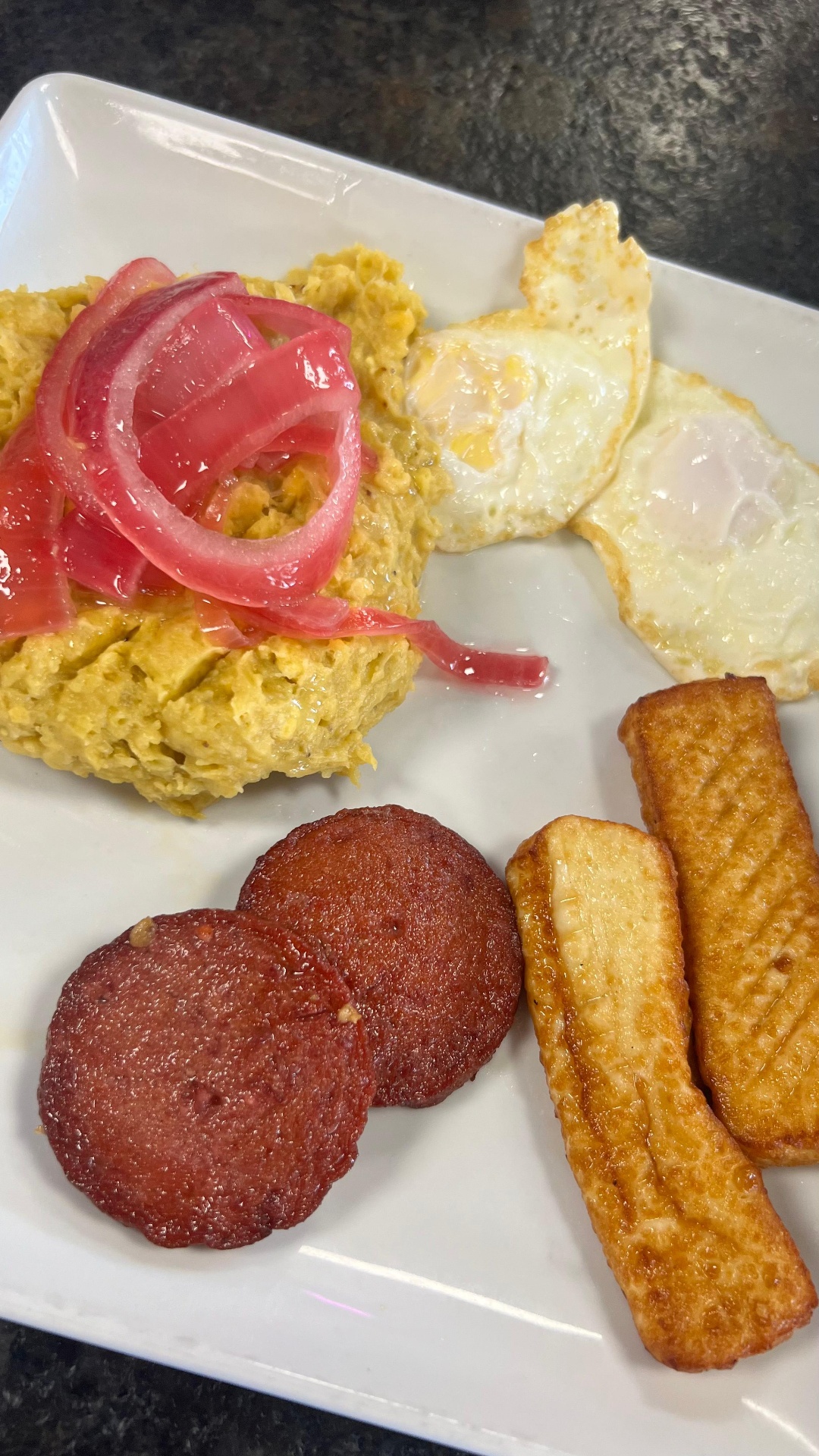 DomiRican brunch plate with mangu, fried eggs, salami, and queso frito topped with pickled red onions