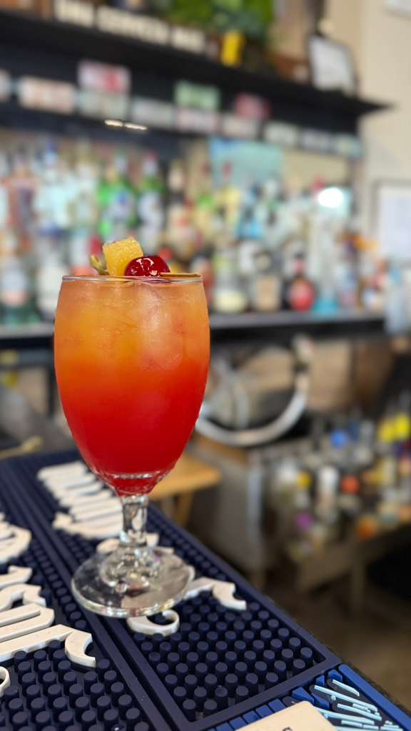 Layered red-to-orange Caribe signature cocktail garnished with cherry and pineapple at the bar