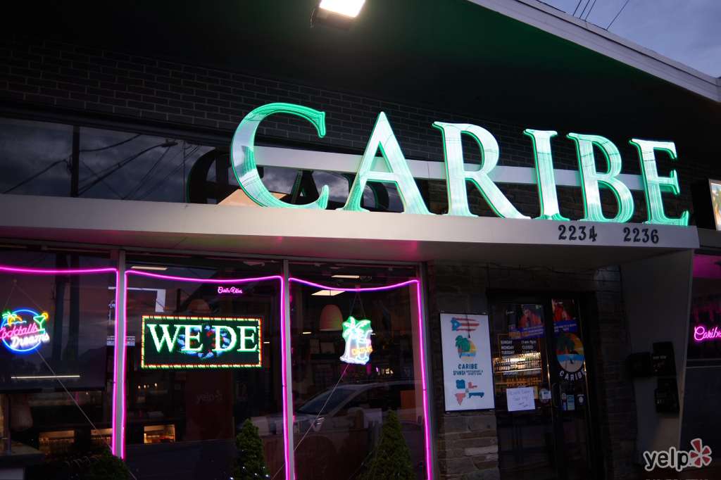 Caribe storefront at night with glowing green CARIBE neon sign and pink neon window trim