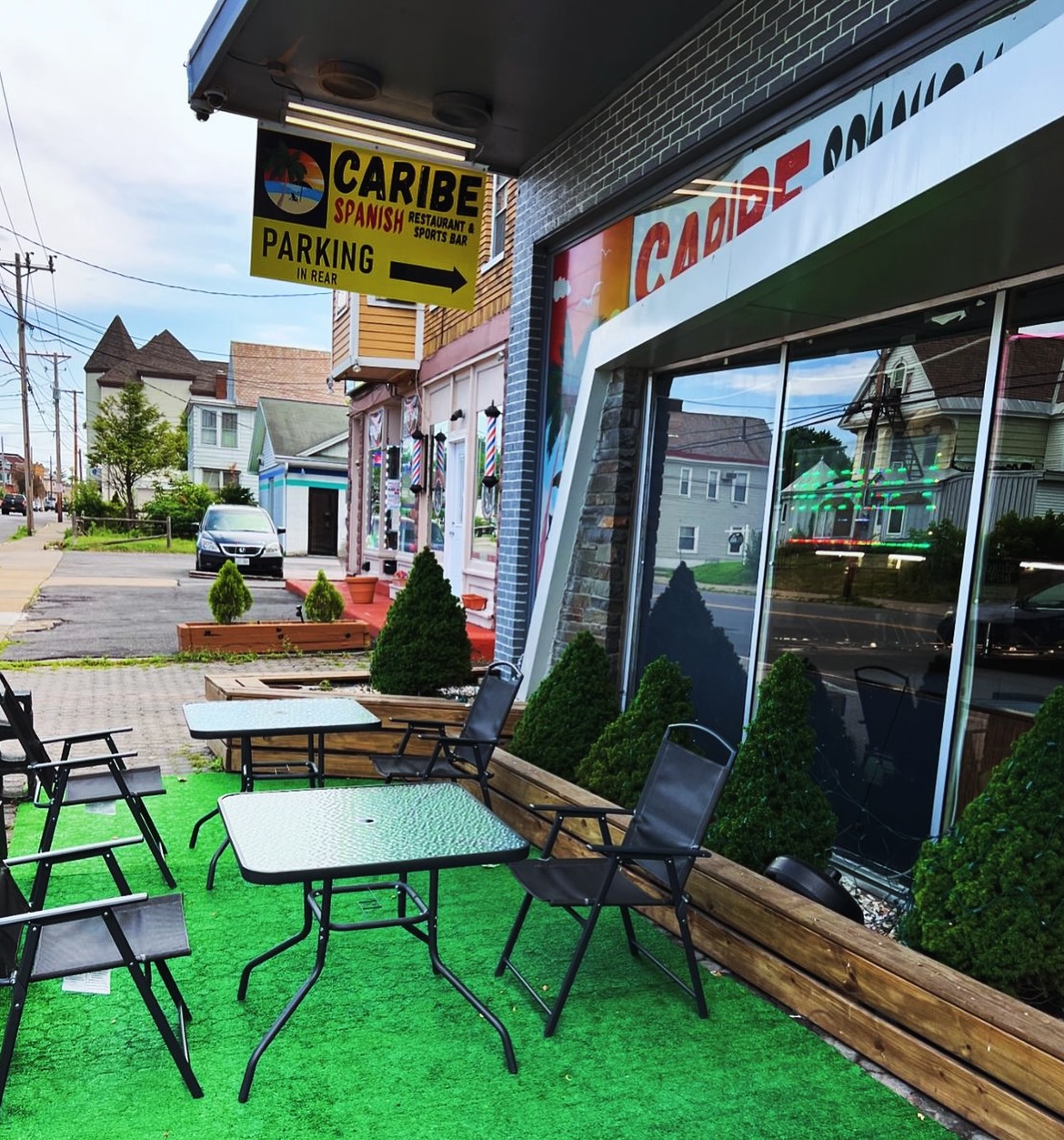 Caribe storefront patio out front with seating, plants, and the green CARIBE neon sign
